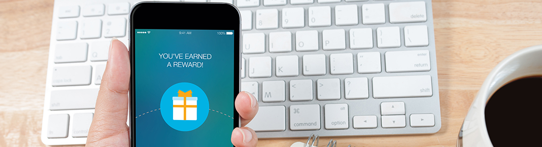 A person holding a smartphone over a keyboard. on the mobile screen there is the message "You've earned a reward"