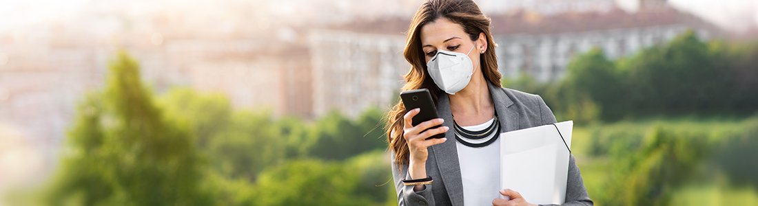 A woman using a mobile device running errands outside wearing a mask